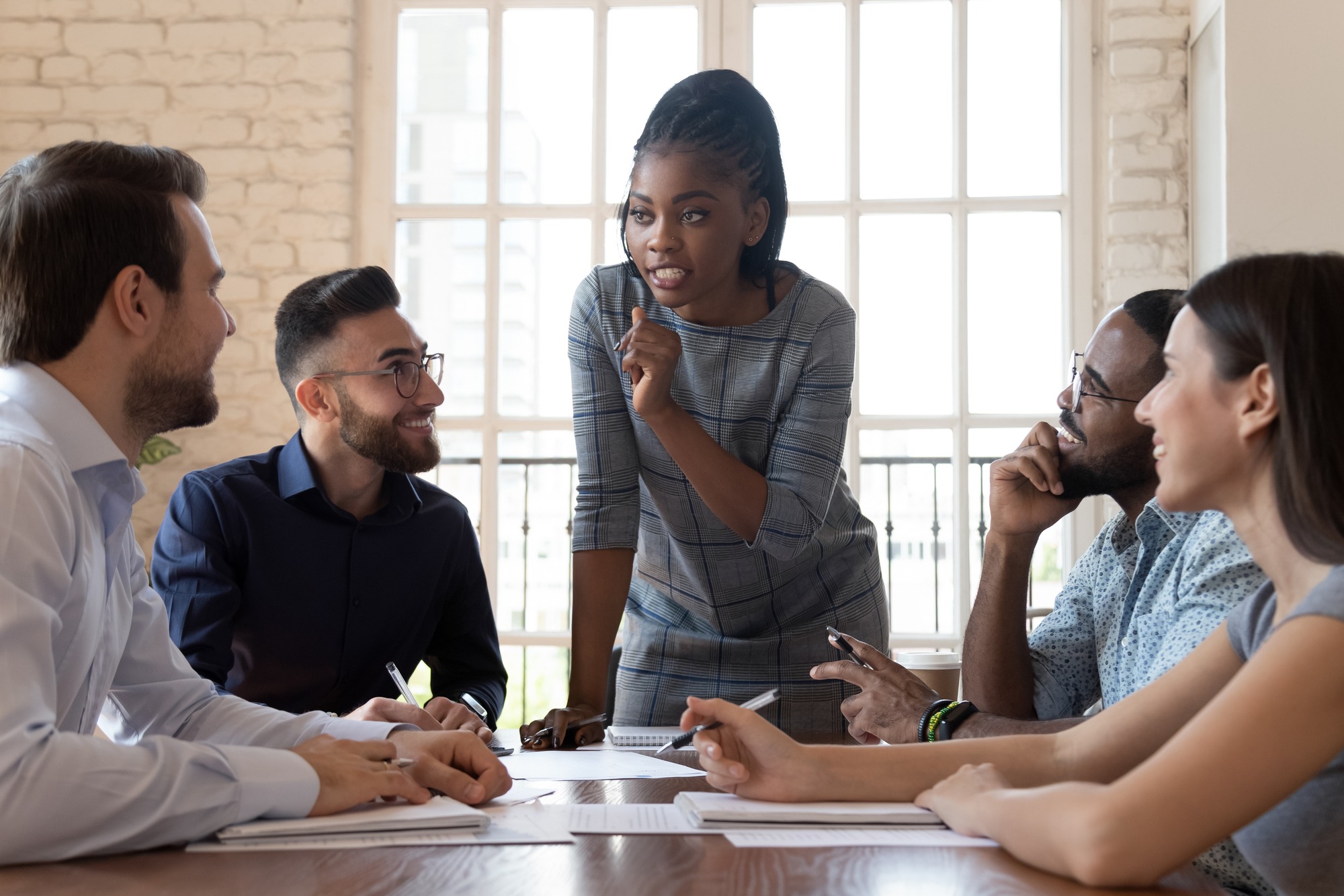 Female black executive leader talking to happy diverse employees group at corporate office briefing, multiracial coworkers listening to african woman boss explain new strategy plan at team meeting.